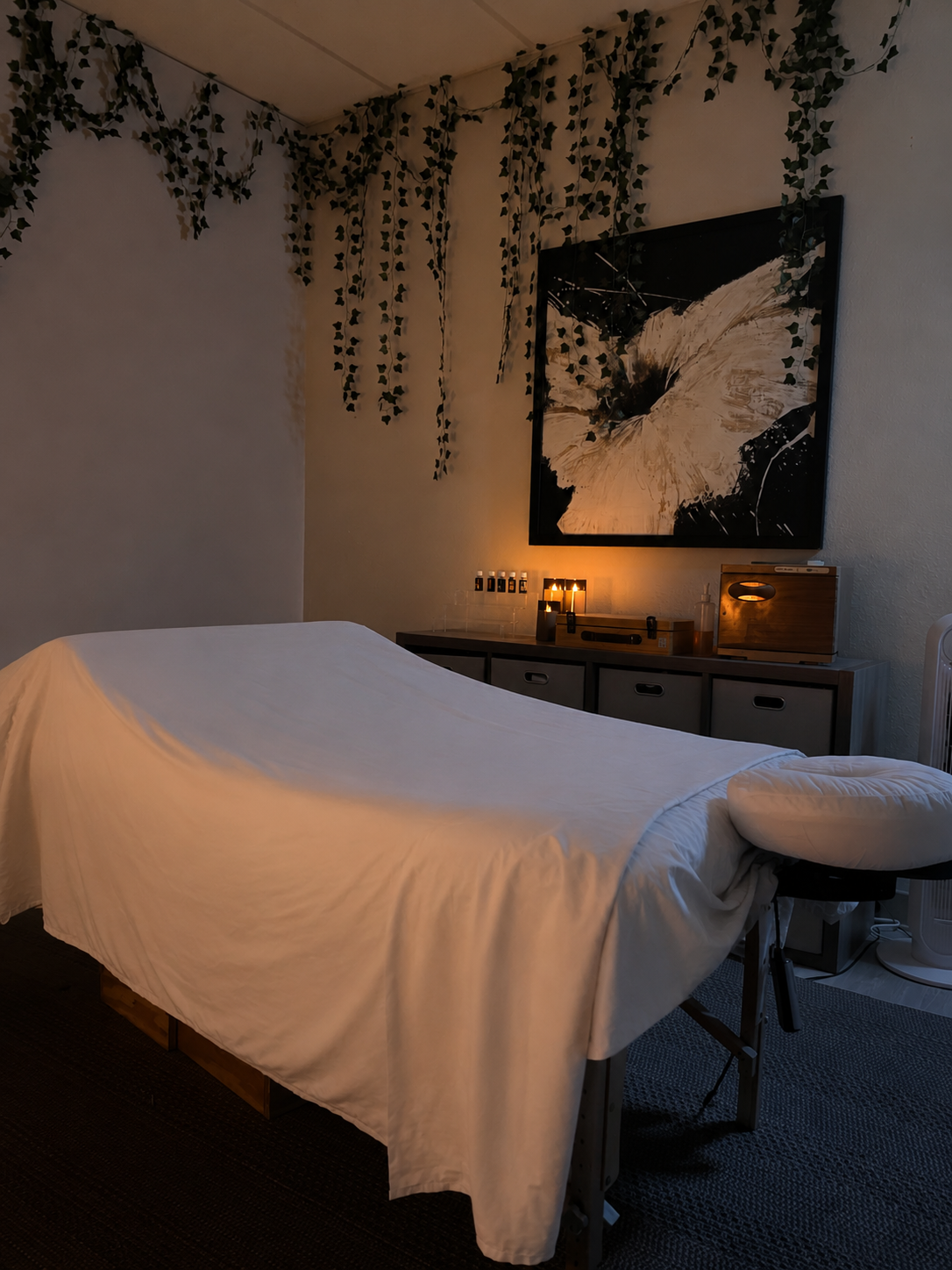 Charlette Evans, LMT treatment room with soft candlelight, hanging ivy, and a dressed massage table
